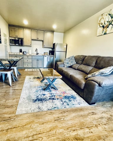 Open-plan living room and kitchen with gray leather sofa, wood flooring, and stainless steel appliances