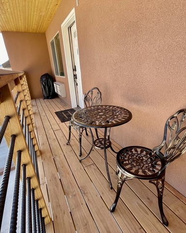 Covered deck with wooden flooring, metal patio furniture, and terracotta stucco building wall