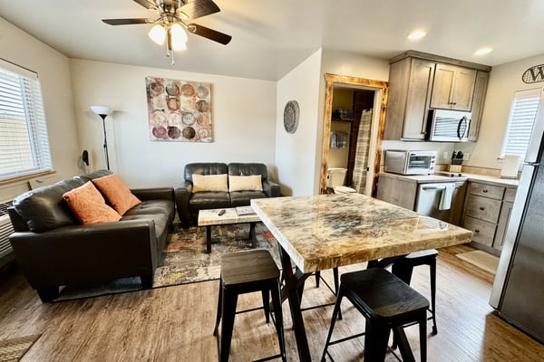 Open-plan living room and kitchen with black leather seating, granite dining table, and wood cabinetry