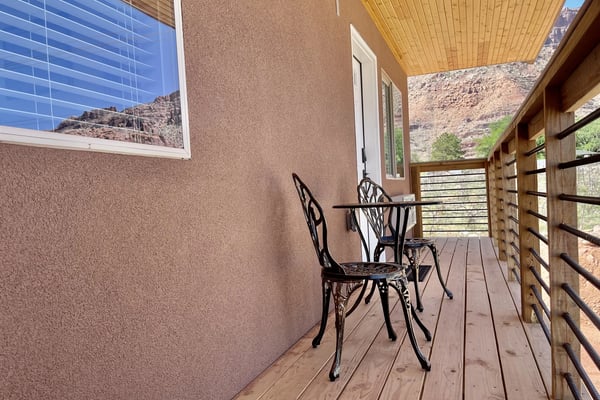 Covered deck with metal chairs and table, wooden railings, mountain views, and yellow ceiling